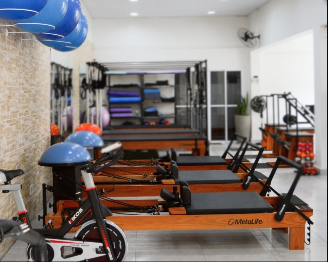Fileira de reformers de Pilates MetaLife em madeira, com bolas suíças azuis na parede de pedra e uma bike ao lado